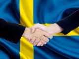 Image of two entrepreneurs with formal suit, shaking hands in front of Sweden national flag